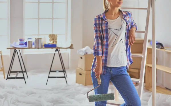 Pretty smiling woman painting interior wall of home with paint roller.