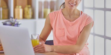 Mutfakta dizüstü bilgisayara benzeyen tariflerle gülümseyen genç bir kadın. Gıda blogcusu kavramı.