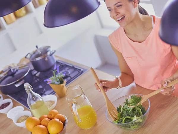 Gülümseyen genç kadın mutfakta taze salata karıştırıyor..