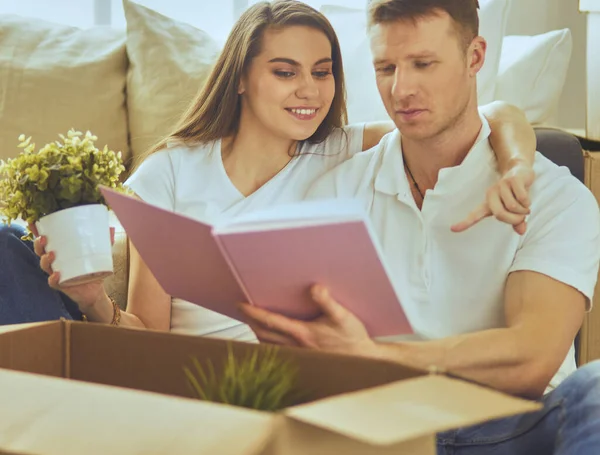 Yeni evlerinde karton kutuları açan sevimli bir çift yerde oturuyor ve bir aile albümüne bakıyor.
