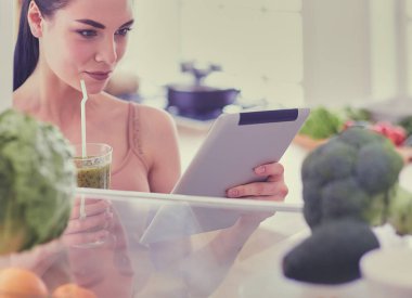 Mutfaktaki masada bir bardak lezzetli, sağlıklı smoothie ile genç bir kadın..
