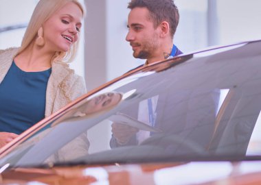 Kadın satıcısı galeride yeni bir arabanın yanında duruyor.