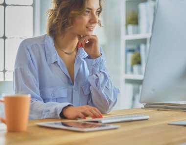 Evdeki bir masada birden fazla cihaz kullanarak çalışan mutlu kadın..