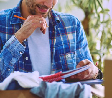 Taşınan bir adam boş bir dairede oturuyor, Kutuların arasında, eşyaların listesini kontrol ediyor.