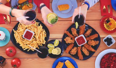 Ahşap masada otururken birlikte yemek yiyen bir grup insanın üst düzey görüntüsü. Masada yemek var. İnsanlar fast food yiyor.