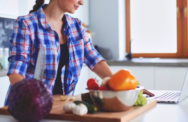 Masanın yanındaki mutfakta sebze doğrayan genç bir kadın..