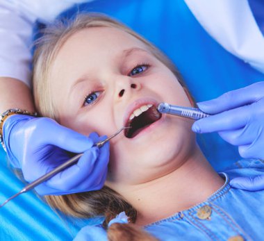 Küçük kız dişçi ofisinde oturuyor.