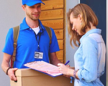 Mavi üniformalı gülümseyen kurye servis konseptine paket kutusu teslim eden teslimatçı. Mavi üniformalı gülümseyen teslimatçı..