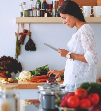 Mutfakta yemek yapmak için tablet bilgisayar kullanan genç bir kadın. .