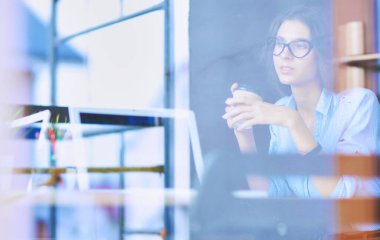 Ofis masasında dizüstü bilgisayarıyla oturan genç bir kadın. Pencereden bakıyor. Genç kadın..