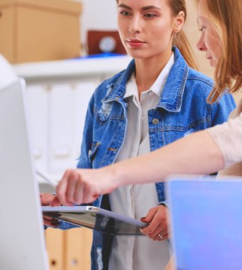 Masanın yanında duran iki genç kadın enstrüman, plan ve dizüstü bilgisayarla