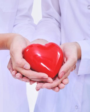 Kırmızı kalp taşıyan iki kadın doktor, beyaz arka planda izole edilmiş..