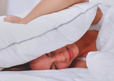 Kadın yatakta yatarken ve yastık, izole kulaklarıyla kapatma