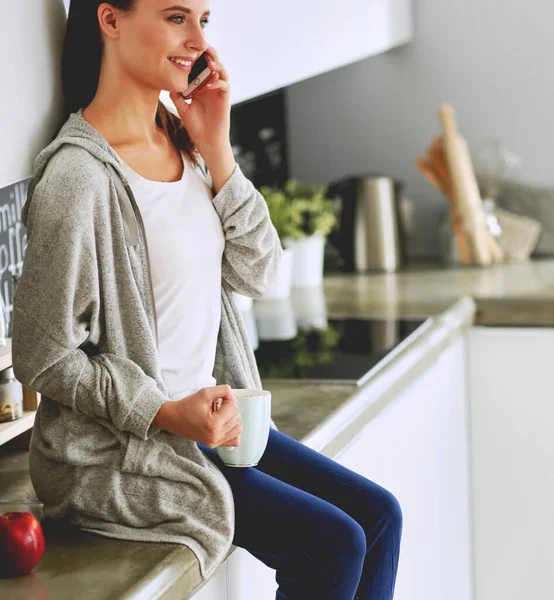 Kobieta Przy Użyciu Telefonu Komórkowego Siedzi Nowoczesnej Kuchni — Zdjęcie stockowe