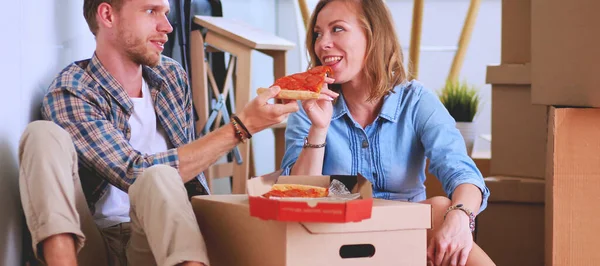 Young couple have a pizza lunch break on the floor after moving into a new home with boxes around them. Young couple.