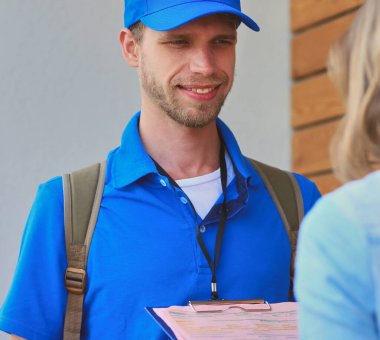 Mavi üniformalı gülümseyen kurye servis konseptine paket kutusu teslim eden teslimatçı. Mavi üniformalı gülümseyen teslimatçı..