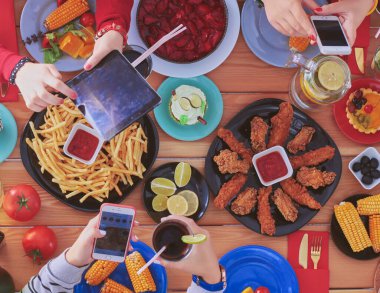 Ahşap masada otururken birlikte yemek yiyen bir grup insanın üst düzey görüntüsü. Masada yemek var. İnsanlar fast food yiyor.