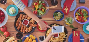 Ahşap masada otururken birlikte yemek yiyen bir grup insanın üst düzey görüntüsü. Masada yemek var. İnsanlar fast food yiyor.