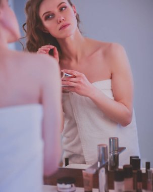 Genç bir kadın aynaya bakıyor ve makyaj yapıyor.