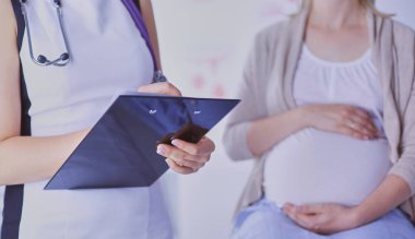 Steteskoplu ve tabletli genç kadın doktor hastanede hamile bir kadınla konuşuyor.