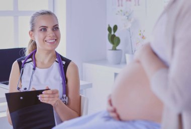 Steteskoplu ve tabletli genç kadın doktor hastanede hamile bir kadınla konuşuyor.
