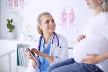 Gülümseyen kadın doktor resimlerini tablette hastanedeki hamile genç bayana gösteriyor..