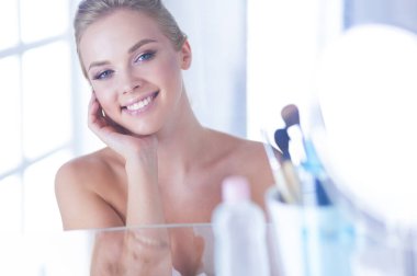 Bornozlu genç kadın banyo aynasına bakıyor..