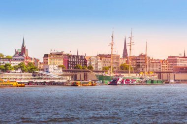 Hamburg, Almanya - 26 Temmuz 2018: Hamburg Elbe nehri, Hamburger Landungsbruecken limanı ve katedral kulesi güzel gün batımı manzarası