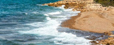 Nature blue turquoise summer sea vacation background banner with waves on stone beach shore close-up