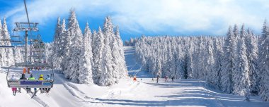Kayak merkezi manzarası, yamaç, kayak asansöründeki insanlar, beyaz çam ağaçları arasında kayakçılar.