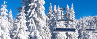 Ski resort with empty chair lift, blue sky and white snowy pine trees at winter sunny day
