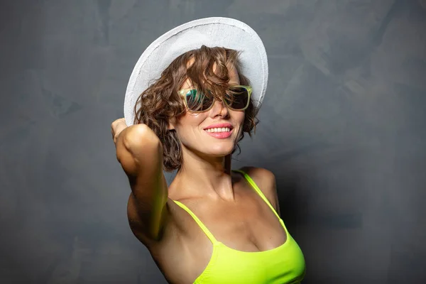 美しいブルネットの女性でカラー水着と飛行髪 コピースペース帽子とサングラスを身に着けている — ストック写真