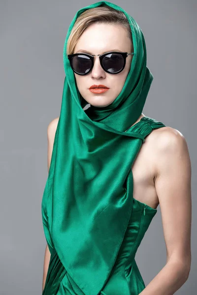 緑の絹のドレスを身に着けている美しい女性 グレーの背景にサングラスとスカーフ — ストック写真