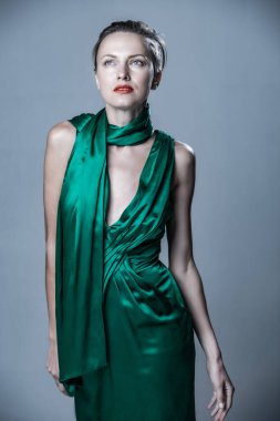 Beautiful woman wearing green silk dress, sunglasses and scarf over grey background