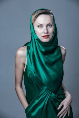 Beautiful woman wearing green silk dress, sunglasses and scarf over grey background