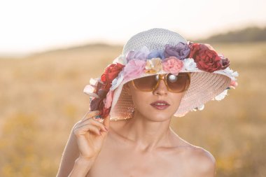 Dışarıda çiçek şapkası ve güneş gözlüğü takan güzel bir kadın.