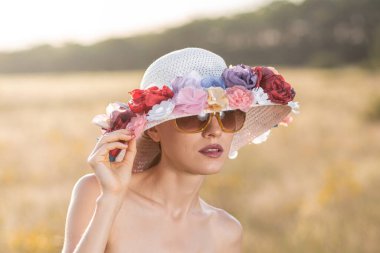 Dışarıda çiçek şapkası ve güneş gözlüğü takan güzel bir kadın.