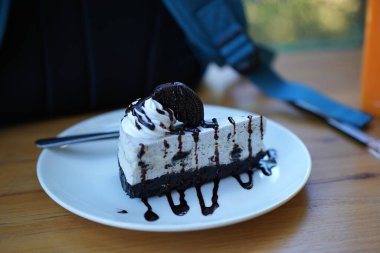 Beyaz plaka ve ahşap masa üzerinde Oreo ve krema ile çikolatalı kek servis etmeye hazır.