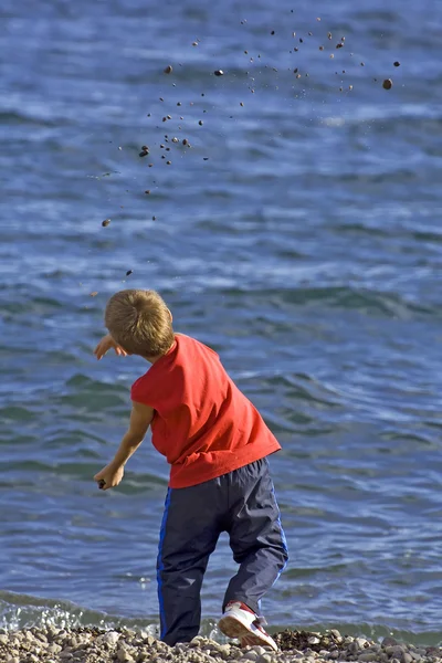 Chlapec házel kamínky do modré moře Royalty Free Stock Obrázky