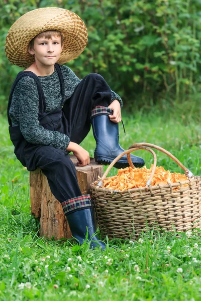 Niño en sombrero de paja se sienta con cesta de cantarelas —  Fotos de Stock