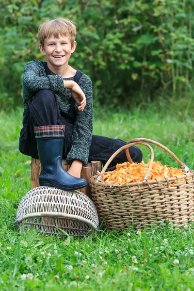 Niño feliz sentado cerca de la cesta llena de cantarelas — Foto de Stock