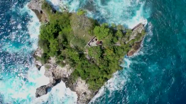 Top-down aerial shot of small isle in Indian ocean, near shore of Nusa Penida Island. Camera slowly move lower, showing rough arid stony surface of submerged rock — Stock Video