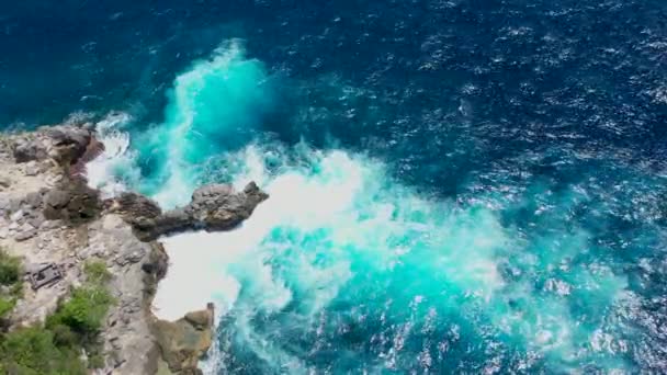 Vista aérea superior de ondas quebrar em rochas em um oceano azul. Ondas do mar na bela praia vista aérea drone 4k tiro. Pássaros vista de olhos de ondas do oceano batendo contra um penhasco de pedra vazia de cima — Vídeo de Stock