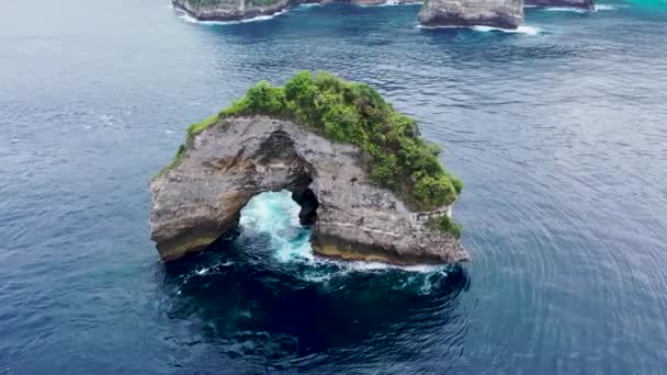 岩の島の周りの回転。ヌサペニダ島の海岸近くのロックバトゥ・メラワンの穴 — ストック動画