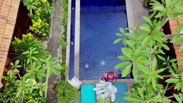 Чоловік середнього віку падає в басейн і бризкає кришталево чистою водою в басейн в сонячний день, літні канікули в тропічному раю — стокове відео