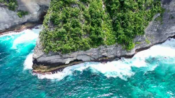 Вид с воздуха с помощью беспилотной камеры в Нуса Пенида, Индонезия. Океан с волнами и скалистой скалой. Бирюзовый водный фон сверху. Летний морской пейзаж из воздуха — стоковое видео