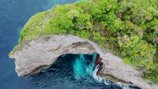 Природная скальная арка в Индийском океане, недалеко от Дикого Побережья на острове Нуса Пенида, Бали. Большое открытое отверстие со стороны скалы образовано волнами. Когда вода попадает в скалу, она создает потрясающий вид. — стоковое видео