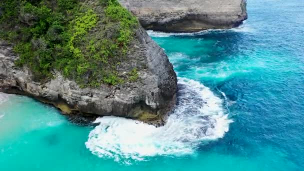 Close up opname van blauwe golven die neerstorten op de tropische rotsachtige kliffen en het zandstrand Top down zicht op turquoise tropische oceaan, kliffen met tropische vegetatie en zandstrand in Bali — Stockvideo