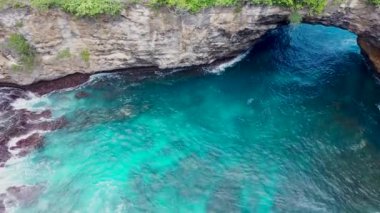 İHA 4K kamerayla hava görüntüsü. Kayalıkları yüksek, dalgalı dalgalı deniz sörfü Nusa Penida, Pasih Uug, Broken Beach. Dalgalar ve kayalık uçurumlarla okyanus. Kuş bakışı