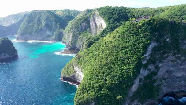 Letecký bezpilotní letoun letí podél útesů, zatímco do nich pronikají vlny z drsného, modrého tropického oceánu. Hinduistický chrám na vrcholu útesu Tanjung Gunungcemeng — Stock video